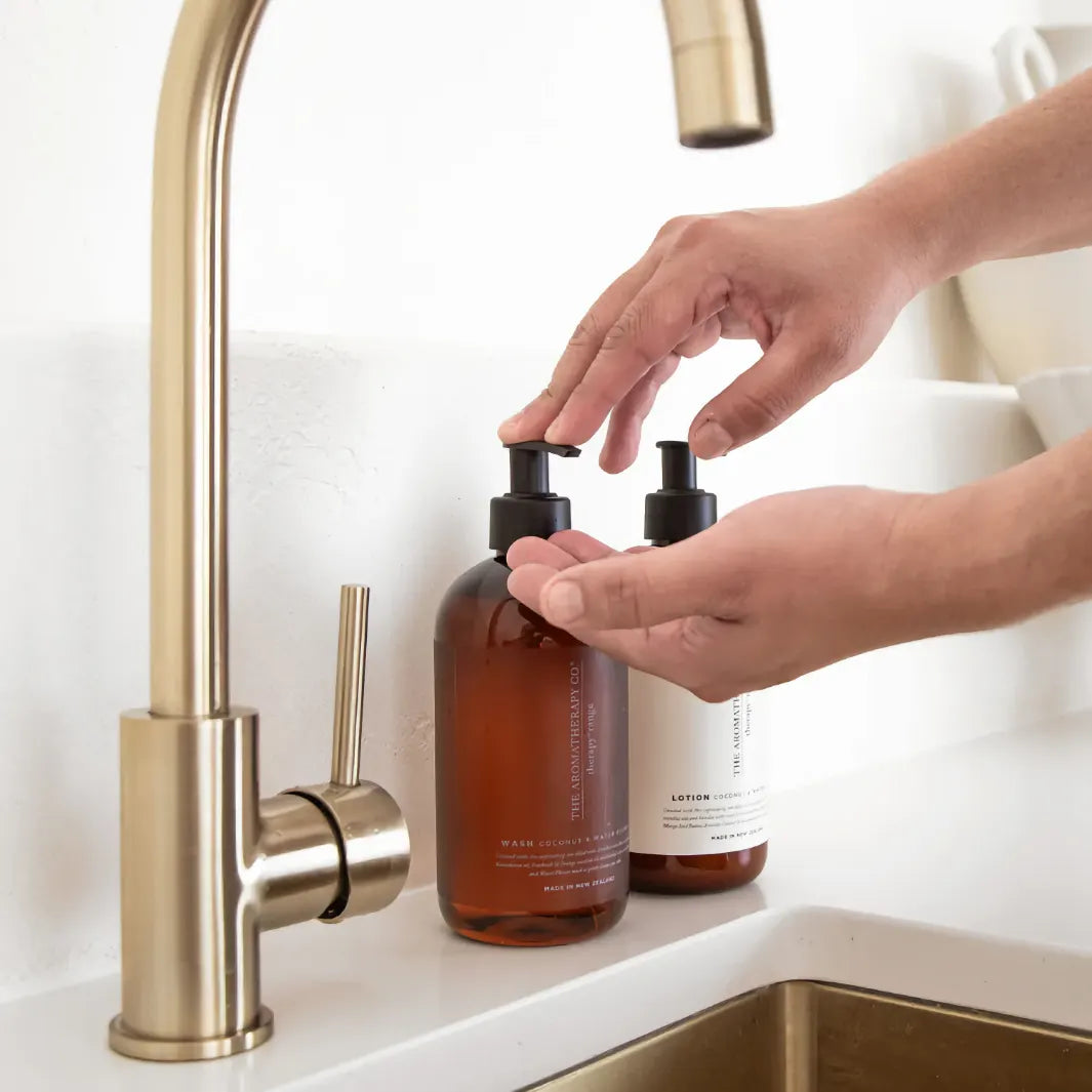 Händer pumpar ut The Aromatherapy Co Wash Cinnamon & Vanilla Bean vid en mässingskran.