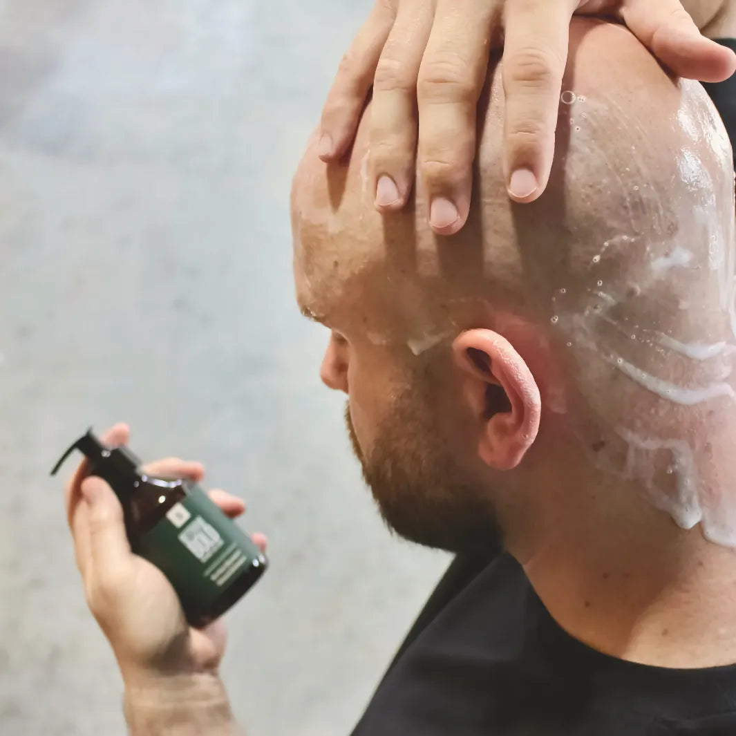 Man masserar in Better Be Bold No Hair Shampoo på rakat huvud – milt schampo som rengör och återfuktar huden
