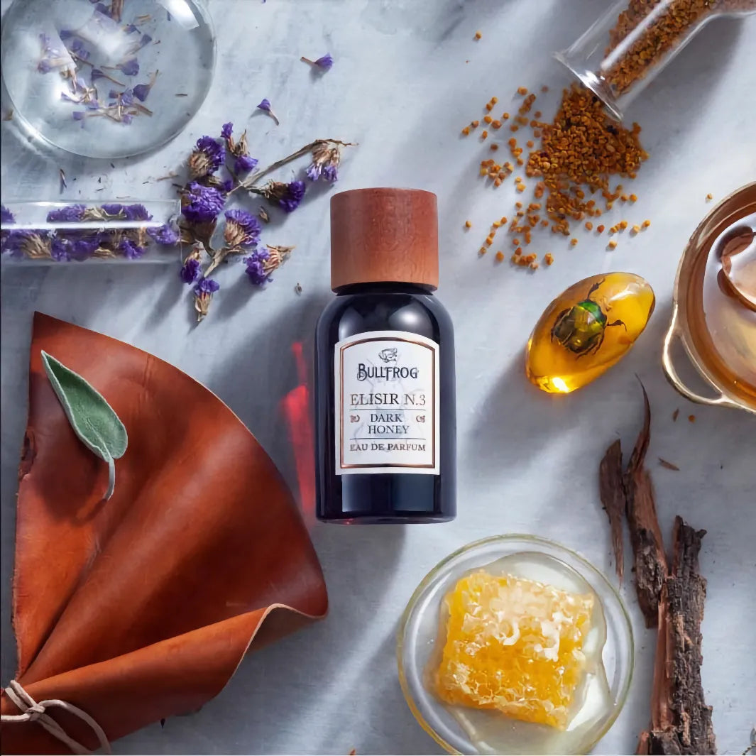 Bullfrog Elisir N.3 Dark Honey EdP placerad på bord med torkade blommor, honungskaka och läderdetaljer – Eau de Parfum för män och kvinnor.