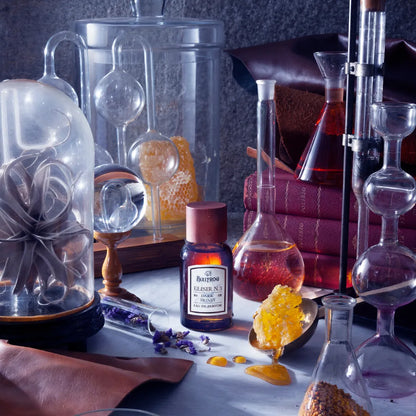 Bullfrog Elisir N.3 Dark Honey EdP parfymflaska omgiven av laboratorieutrustning, böcker och honung - en doft med läder, ros och bärnsten.